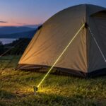 夕暮れのキャンプ場でテントから反射するガイロープを張った様子