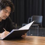 稽古場で台本ファイルを開き、鉛筆で書き込む演劇講師