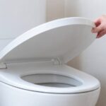 白いトイレの便ふたを手で持ち上げている様子