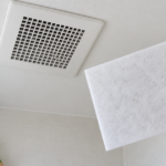 トイレ天井の換気口と白い交換用フィルターを手に持つ様子