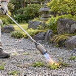 砂利の雑草に長柄の草焼きバーナーを向けている様子