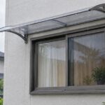 雨天の住宅で窓の上に透明な後付けひさしが設置されている様子