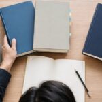 複数の専門書とノートを机に広げて学習している様子